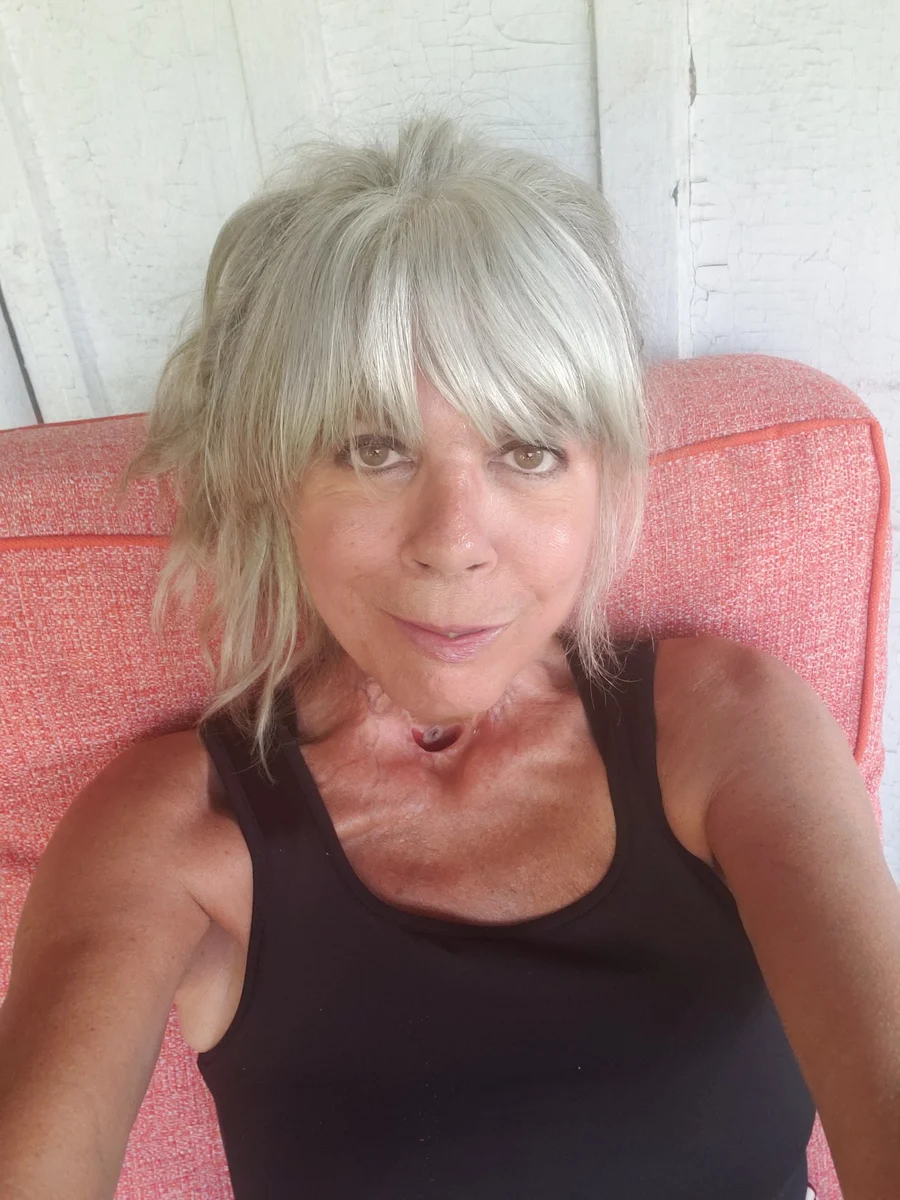 Vivienne seated against a coral-coloured cushion, wearing a black sleeveless top.